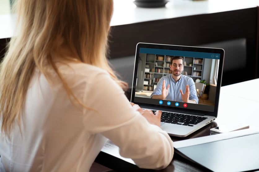 Woman sitting at computer talking to man on screen